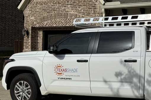 White Texas Shade work truck with a ladder rack parked in front of a brick home, the door showing the logo and "Serving DFW since 2012"