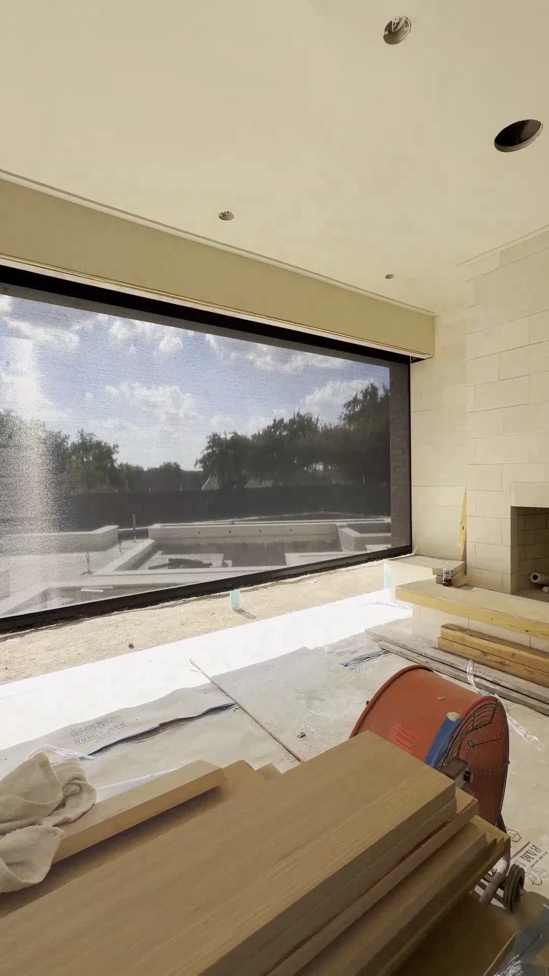 A motorized shade lowered from a recessed ceiling pocket across a wide opening in a home under construction