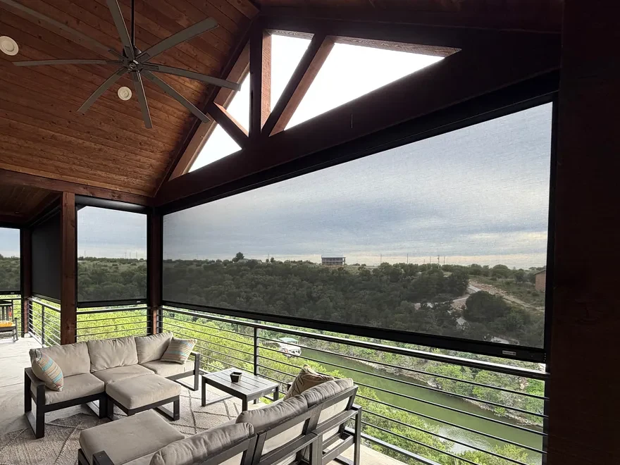 Lowered patio screen on a covered porch, with a wooded hillside visible through the mesh and green water below