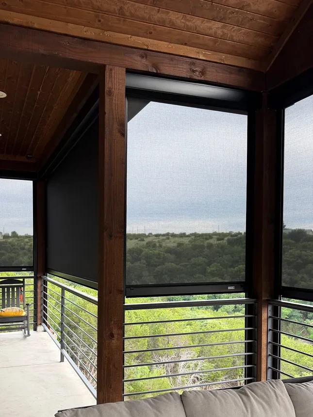 Wood-beam porch with motorized screens lowered over several openings, looking out to wooded hills