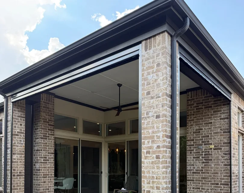 Corner of a brick home's covered patio in Colleyville with the shades raised into the headers above the openings