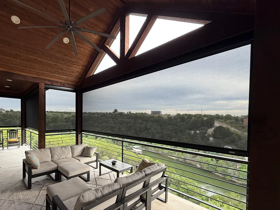 Lake-home porch in Graford with a motorized shade lowered over the cove view, a sectional on a rug and a ceiling fan