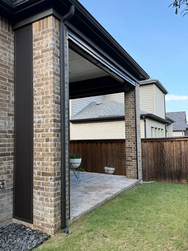 Brick column on a Colleyville patio with a dark vertical side track beside a downspout and the header above the opening
